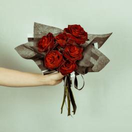 Handheld bouquet of red roses wrapped in dark brown paper