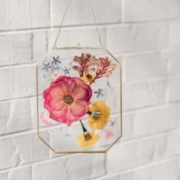 Framed pressed flowers in a hanging glass and brass display