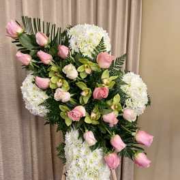 Standing white floral cross with pink roses and green orchids on a wooden easel