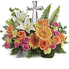 Mixed arrangement of lilies, roses, and gerbera daisies with a silver cross in the center