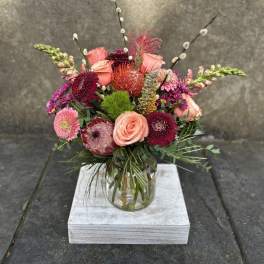 Mixed pink and burgundy flowers arranged in a glass vase