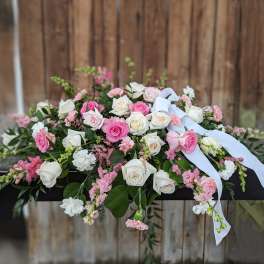 Pink and white rose arrangement with ribbon draped over a dark casket