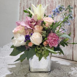 Mixed bouquet in a square glass vase with roses, lilies, and blue flowers