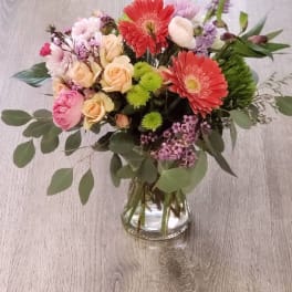 Mixed bouquet of pink, peach, and red flowers in a glass vase