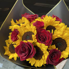Bouquet of yellow sunflowers and red roses wrapped in black paper with gold trim.