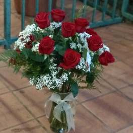 Arrangement of red roses with white filler flowers in a clear glass vase tied with a sheer bow.