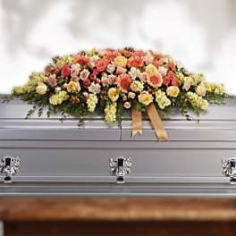 Peach and yellow casket spray of roses and mixed blooms with ribbon on a silver casket