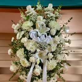Tall white sympathy standing spray with roses, lilies, and mums accented by a white ribbon bow