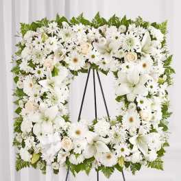 White floral wreath on a black easel with lilies, daisies, and roses