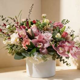 Low arrangement of pink orchids and roses with white and peach blooms in a white ceramic cylinder vase