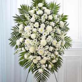 Large white funeral spray with mixed blooms and palm fronds on a stand