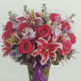 Bouquet of red roses and pink lilies in a clear glass vase with a purple ribbon