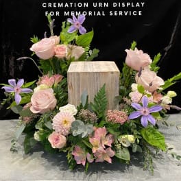 Floral cremation urn display with pink roses and purple clematis around a wooden urn box