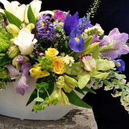 Mixed bouquet in a white container with blue, yellow, and purple flowers