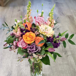 Mixed bouquet of roses, snapdragons, and purple blooms in a glass vase
