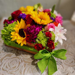 Colorful mixed bouquet with sunflowers, red roses, and pink blooms in a wooden box