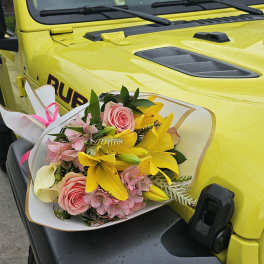 Bouquet of pink roses, yellow lilies, and pale pink flowers wrapped in white paper