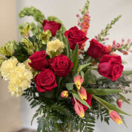 Bouquet of red roses, yellow carnations, and pink tulips in a glass vase