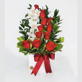 Red roses and white orchids arranged in a white vase with a red ribbon