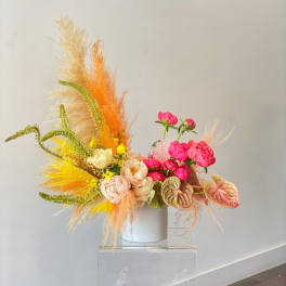 Bright floral arrangement with pink blooms and orange feathery accents in a white vase