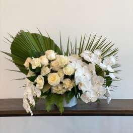 White roses and orchids arranged in a low vase with palm leaves