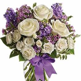 White roses and purple flowers in a glass vase with a purple ribbon
