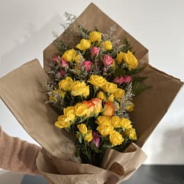 Bouquet of yellow and pink roses wrapped in brown paper with a pink ribbon
