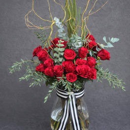 Red roses in a clear glass vase with black-and-white ribbon