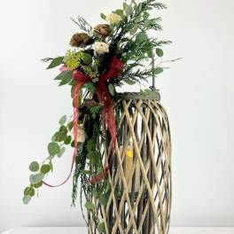 Tall floral arrangement in a woven lantern-style vase with red ribbon