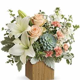 Bouquet of white lilies, peach roses, and pink carnations in a wooden cube vase