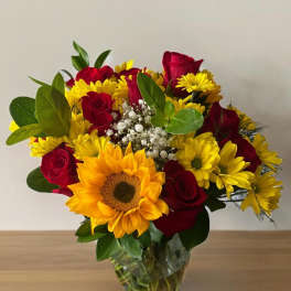 Bouquet of red roses and yellow sunflowers in a clear glass vase