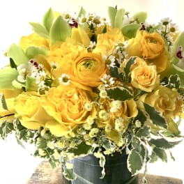 Yellow roses and ranunculus in a glass vase with small white daisies