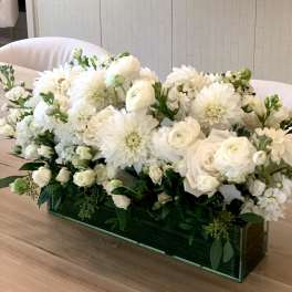 Low rectangular arrangement of white roses, dahlias, and other blooms in a green glass vase