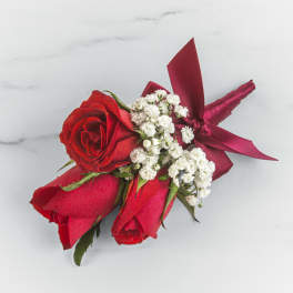Three red roses with white filler flowers and a red ribbon corsage
