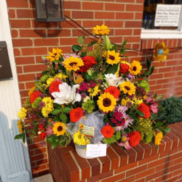 Large mixed bouquet of sunflowers, roses, and lilies in a white container