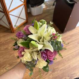 Handheld bouquet of white lilies, pink roses, and purple flowers