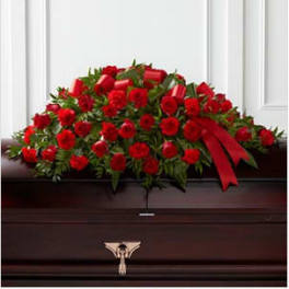 Red rose casket spray with a red ribbon on a dark wood casket