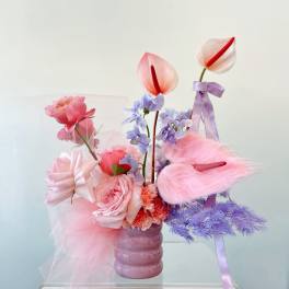 Pink and lavender floral arrangement in a mauve vase with ribbon accents