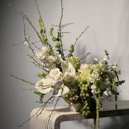 White floral arrangement with orchids, roses, and green grapes in a vase