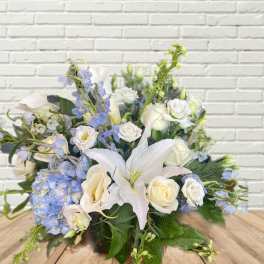 White lilies, calla lilies, roses, and blue flowers in a low arrangement