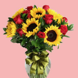 Bouquet of red roses and yellow sunflowers in a glass vase with a ribbon