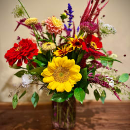 Mixed bouquet with a yellow sunflower and red and pink blooms in a clear glass vase