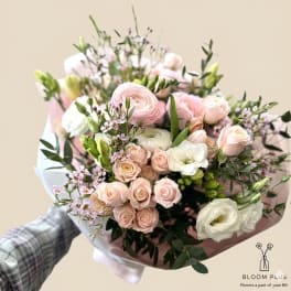 Handheld bouquet of pale pink and white flowers wrapped in pink paper