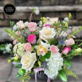 Basket arrangement of white and pink roses with hydrangeas and accent blooms.