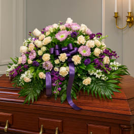 Purple and cream floral casket spray with ribbon on a wooden casket