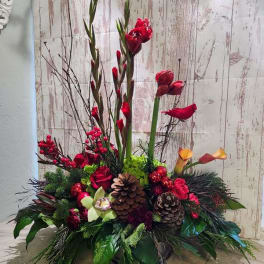 Tall floral arrangement with red blooms, calla lilies, and pinecones