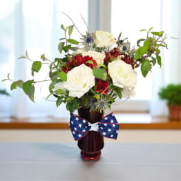 Patriotic red, white, and blue flower arrangement in a red vase with a star-spangled bow.