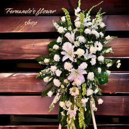 Tall standing spray of white lilies, roses, carnations, and mums with green accents on a wooden backdrop