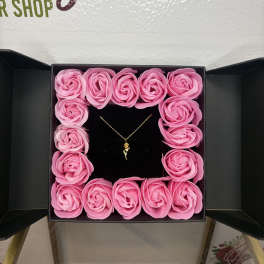 Pink rose-shaped flowers arranged in a square gift box with a necklace in the center.