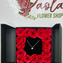 Box of red roses with a small heart necklace in the center